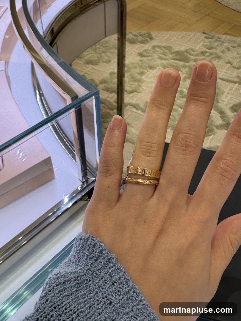 A close-up shot of a person's hand wearing two gold rings. The rings appear to be engraved with text and small diamonds. The background shows a blurred display case and a rug.