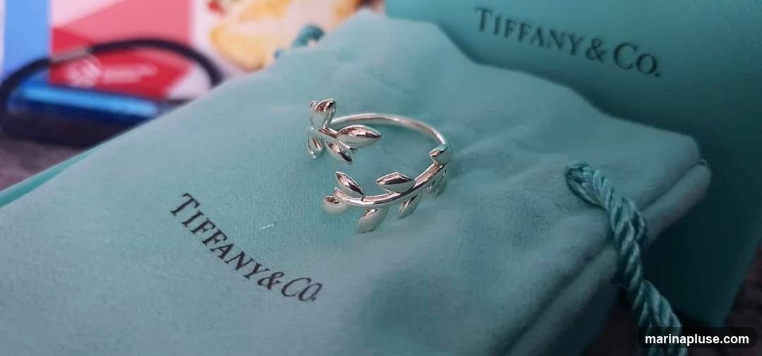 A silver ring with a leaf motif rests on a teal Tiffany & Co. pouch. A Tiffany & Co. box is visible in the background.