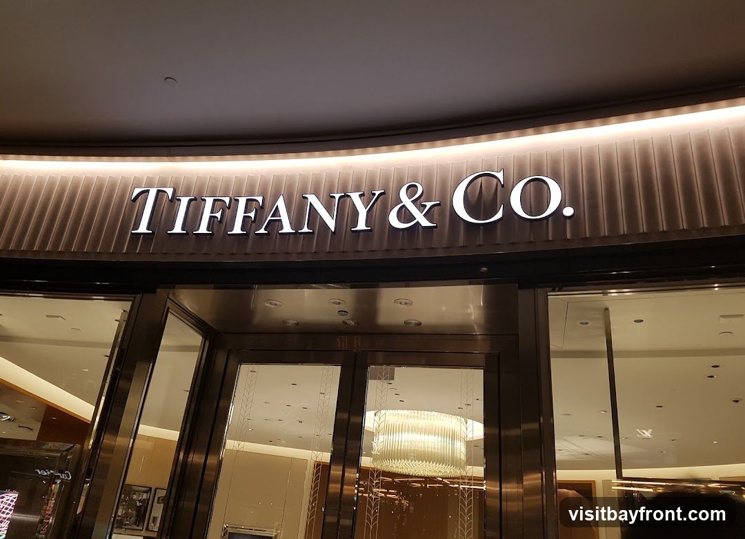 The illuminated sign for Tiffany & Co. is prominently displayed above the entrance of the store. The entrance features large glass doors and windows, reflecting the interior lighting and decor.