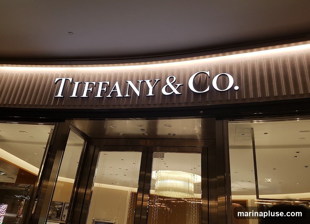 The illuminated sign for Tiffany & Co. is prominently displayed above the entrance of the store. The entrance features large glass doors and windows, reflecting the interior lighting and decor.