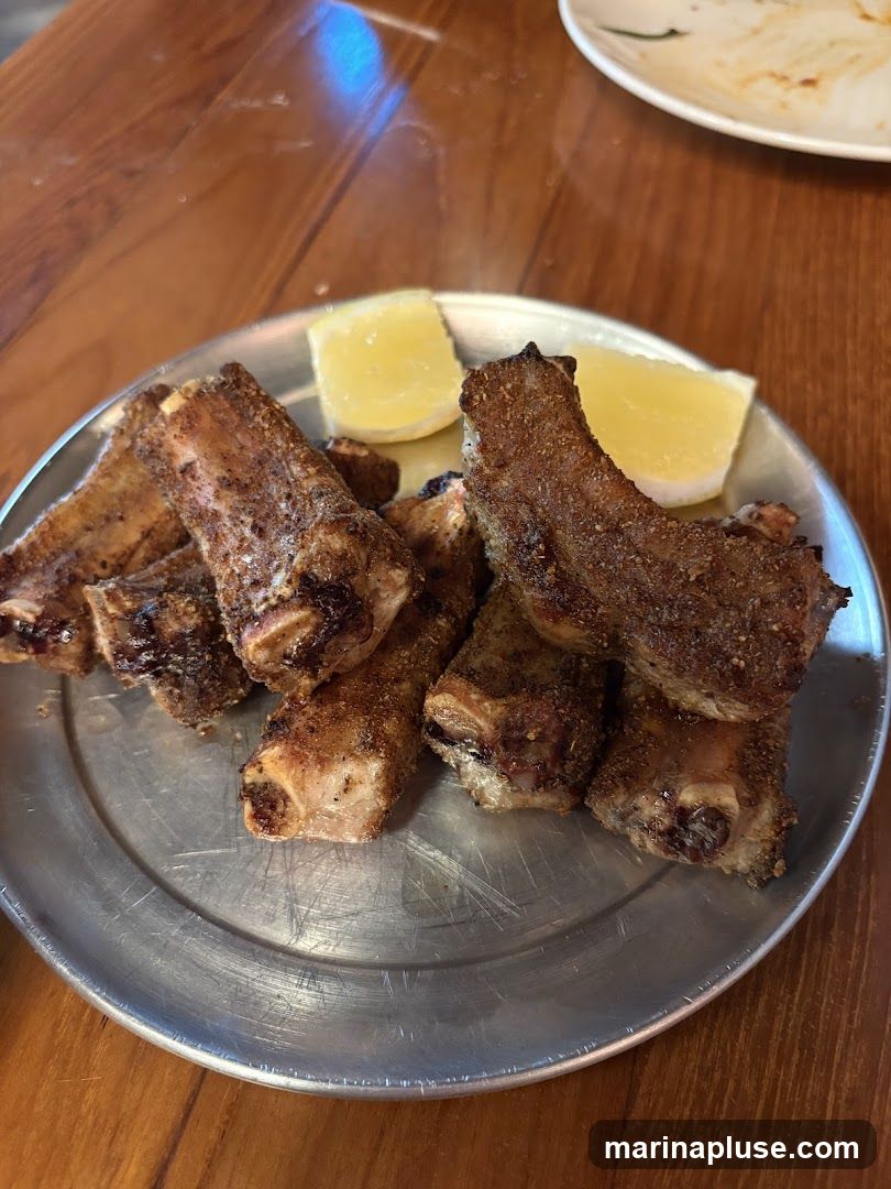 A metal plate filled with several cooked ribs, seasoned with spices, and garnished with three lemon wedges. The plate rests on a wooden table.