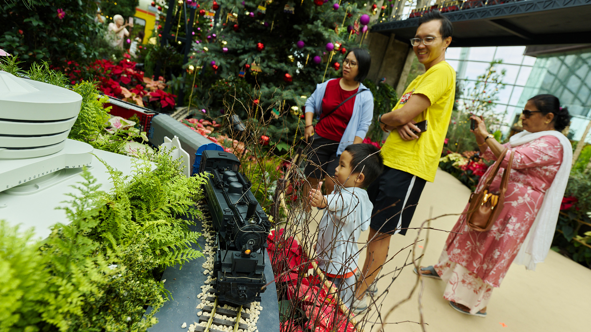 Visitors watching a model locomotive beside poinsettias inside Flower Dome, Gardens by the Bay